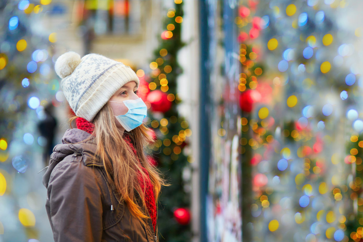 Masked woman looking at store window with holiday lights and decor